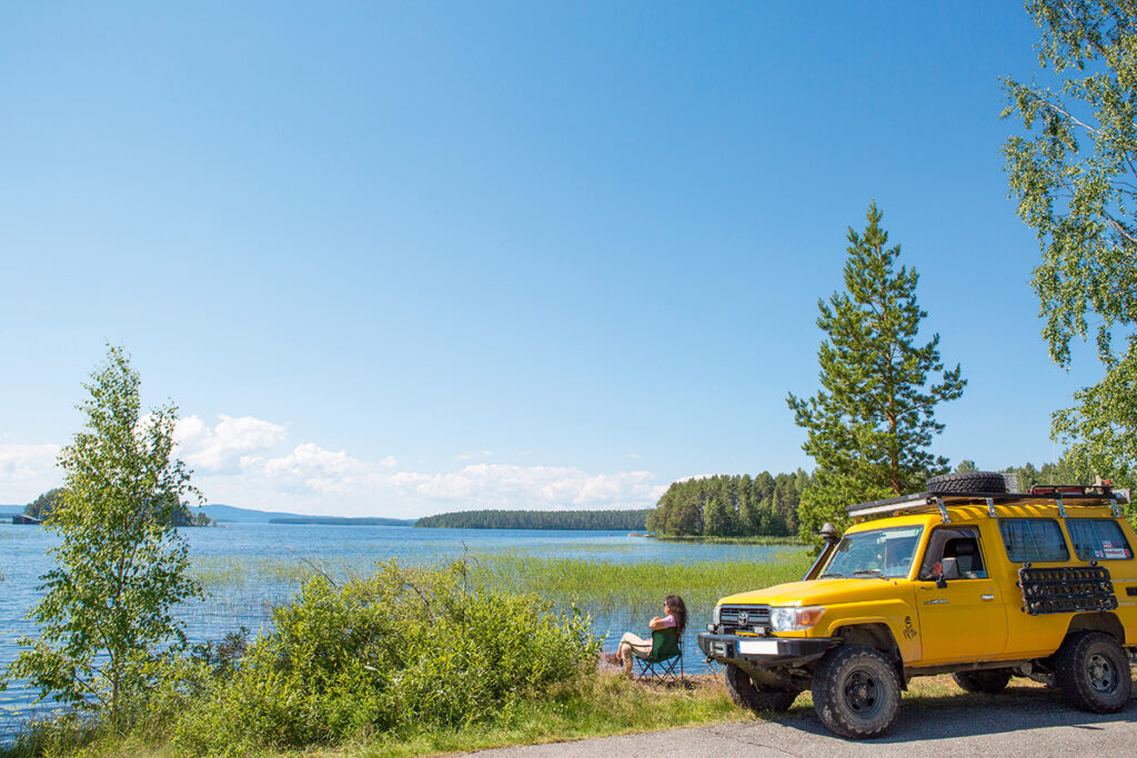 Finnland Pielinenroute Frau vor einem gelben Camper am See