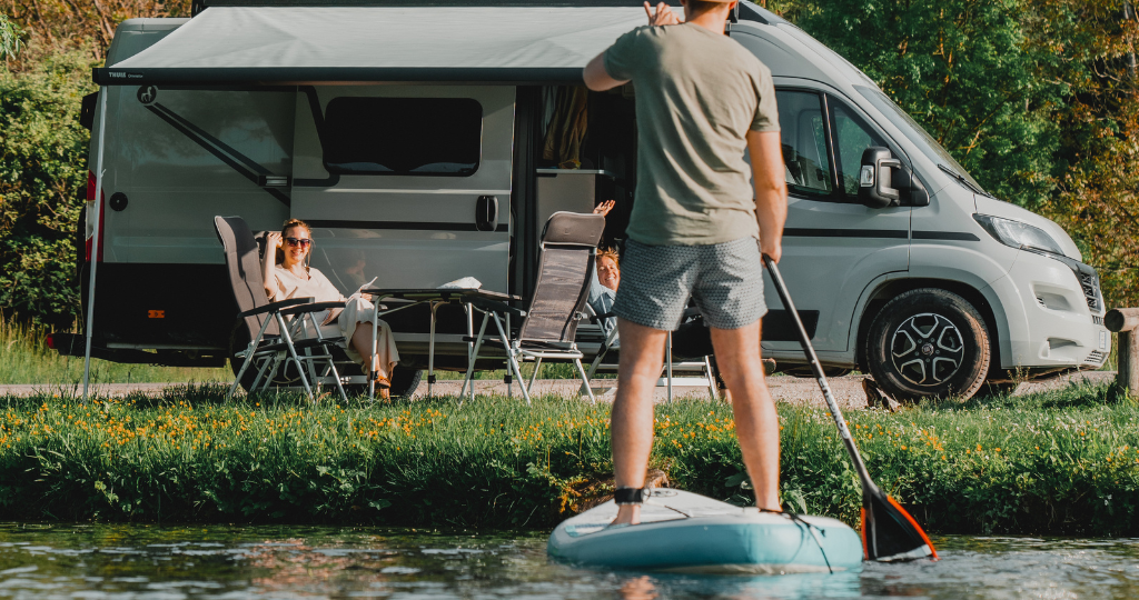 SUP Paddler vor einem Etrusco Wohnwagen, vor dem eine Frau sitzt