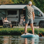 SUP Paddler vor einem Etrusco Wohnwagen, vor dem eine Frau sitzt