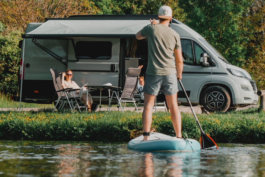 SUP Paddler vor einem Etrusco Wohnwagen, vor dem eine Frau sitzt